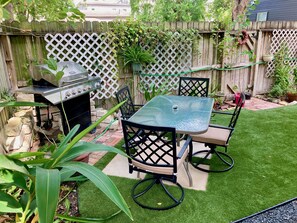 A backyard with a grill, a table, chairs, and a small garden area.