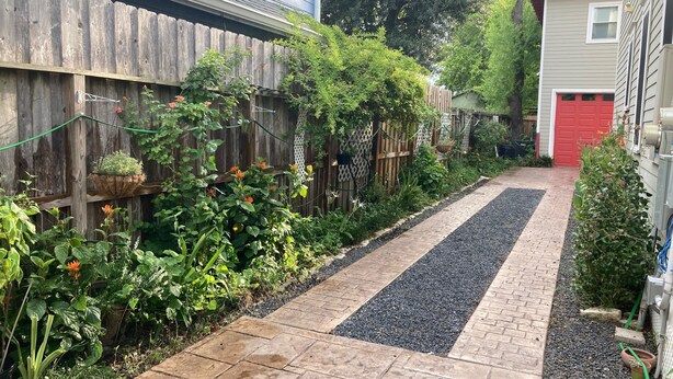 Uma trilha no jardim com cerca de madeira e diversas plantas.