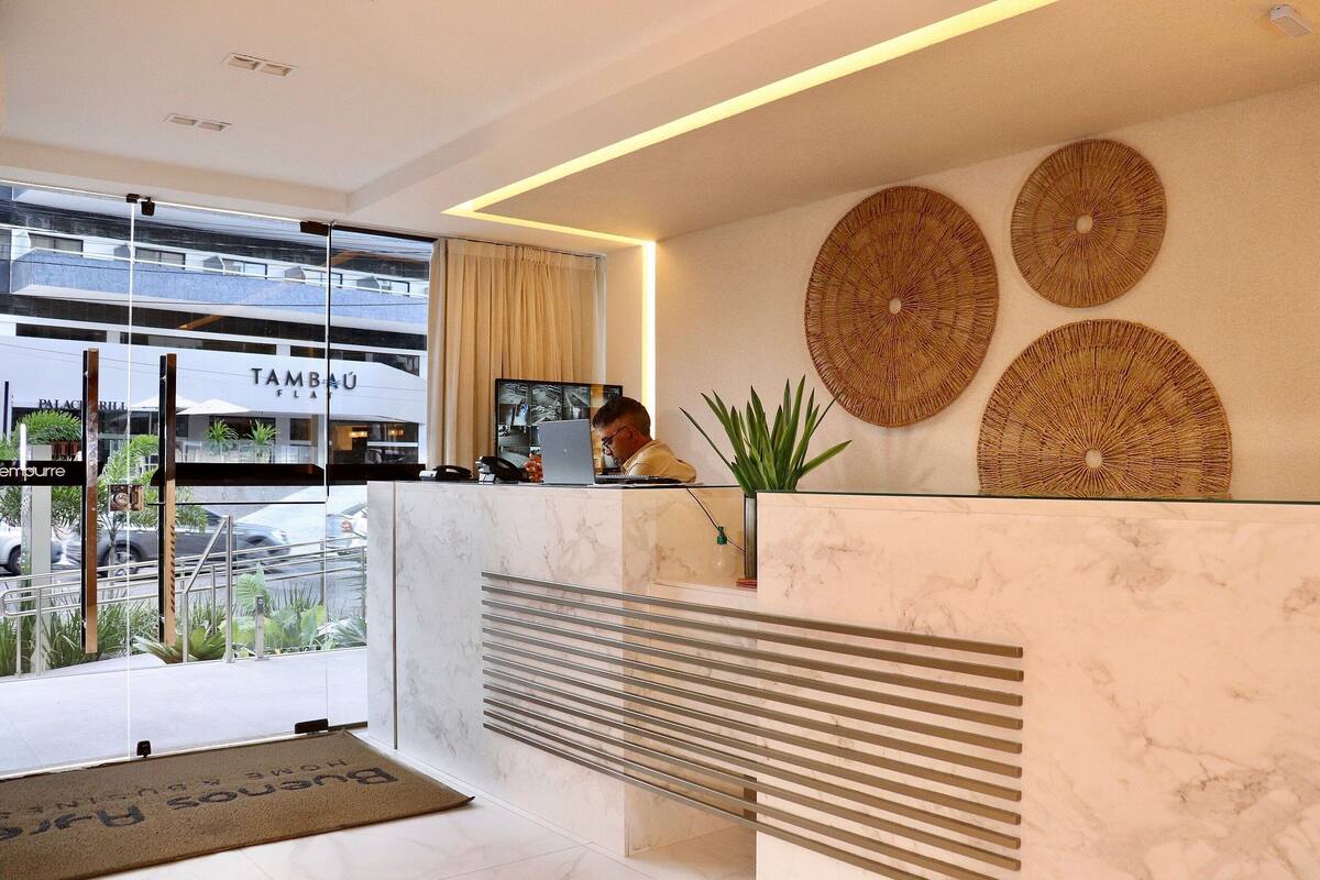 Zona de recepción de un hotel con diseño moderno, que incluye un mostrador de mármol, una pantalla grande y arte decorativo de fibras en la pared.