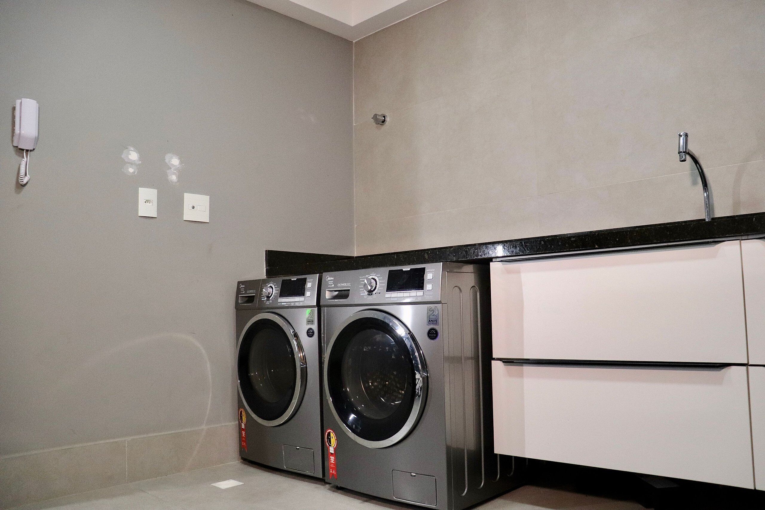 A laundry area with two front-loading washing machines, a black countertop, and a white cabinet.