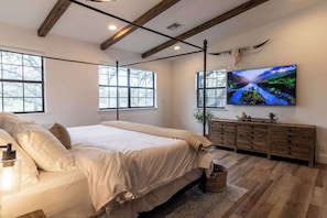 A bedroom with a large bed, wooden floor, a TV on the wall, and a rustic decor theme.