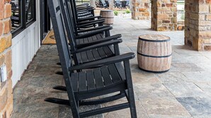 A covered outdoor seating area with black rocking chairs and stone pillars. - Raymond Ranch Main House - Sleeps 14 (9 beds) - Fredericksburg Texas Finest (Fredericksburg)