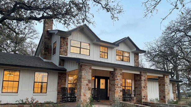 A two-story house with a stone facade, large windows, and a front porch with chairs. - Raymond Ranch Main House - Sleeps 14 (9 beds) - Fredericksburg Texas Finest (Fredericksburg)