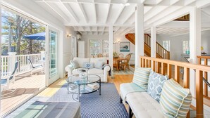 A spacious living area with a large glass door leading to a deck, a cozy seating area with a sofa and chairs, and a staircase connecting to another level. - Lovely Beach house in GRB - Heated pool! (Kennebunk)