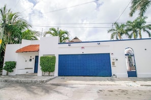A white building with a blue garage door, a red-tiled roof, and a gated entrance.