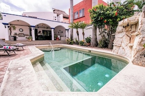 A swimming pool with a stone wall and a patio area with lounge chairs.