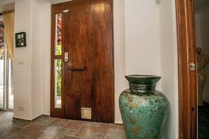 A wooden door with a glass panel, a large vase, and a statue in the background. - Tropical retreat with beautiful pool and yard (San Miguel de Cozumel)