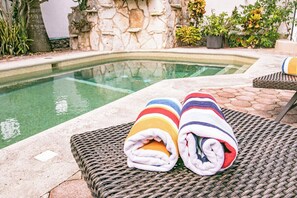 Un espace aménagé au bord de la piscine, avec un mur en pierre et un fauteuil de relaxation en osier.