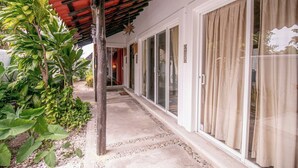 A covered walkway with a tiled floor, surrounded by lush greenery and a glass door entrance. - Tropical retreat with beautiful pool and yard (San Miguel de Cozumel)