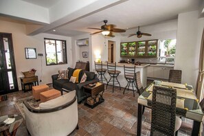 Un salon comprenant un canapé, des poufs, une table basse en verre et un coin repas avec une table et des chaises en verre.