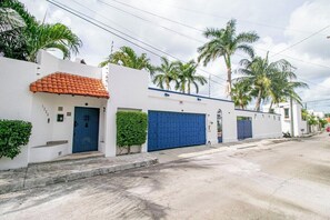 Een woonstraat met witte huizen, blauwe garage deuren en palmbomen.