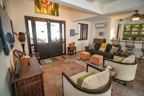 A living room with a sofa, ottomans, a coffee table, and a dining area with chairs. - Tropical retreat with beautiful pool and yard (San Miguel de Cozumel)