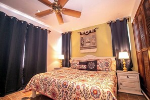 A bedroom with a bed, two bedside tables, a ceiling fan, and curtains.