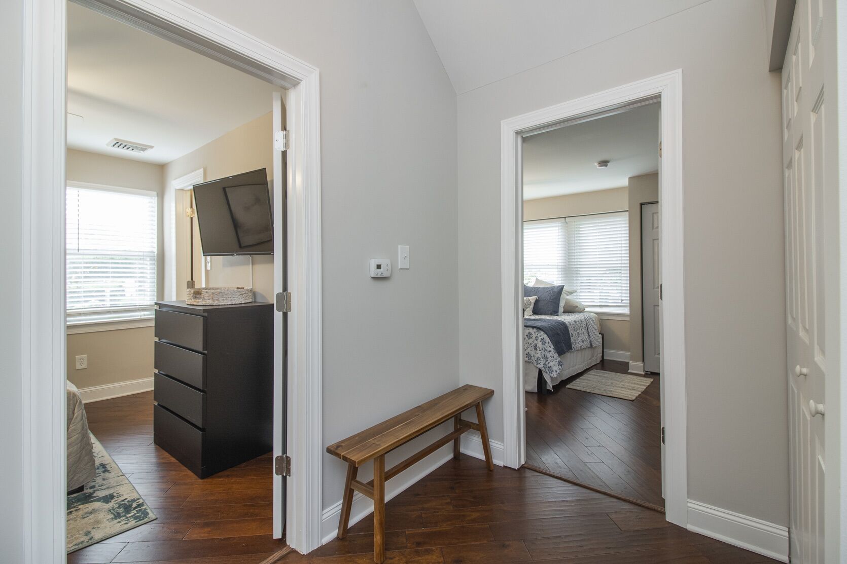 A hallway with a wooden bench, a dresser, and a bed with a window.