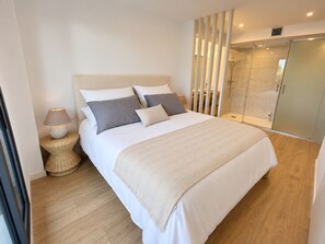 A modern bedroom with a large bed, a bedside lamp, and a glass shower enclosure.