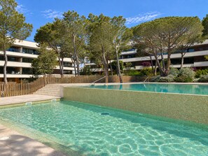 A swimming pool with a wooden deck and steps leading into it, surrounded by trees and modern buildings.