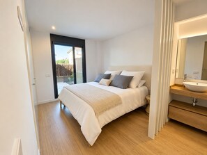 A bedroom with a bed, a bathroom with a sink, and a sliding glass door to a balcony. - Apartamento Nuevo, Equipado y Decorado con Estilo (Palamós)