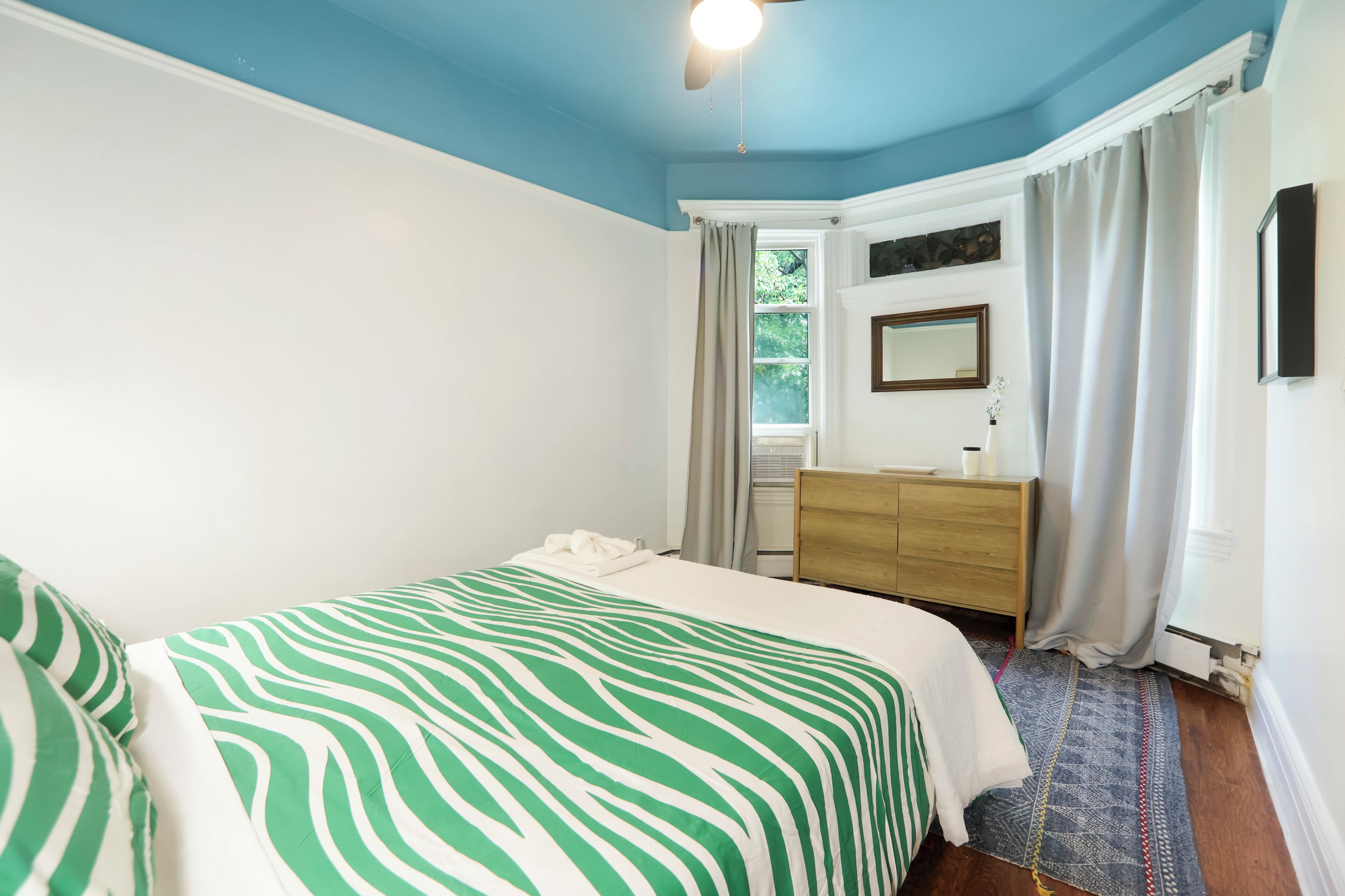 Un dormitorio con cama, cómoda, espejo y ventana con cortinas.