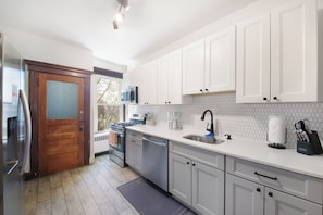 Une cuisine moderne avec des armoires blanches, des appareils en acier inoxydable et une porte en bois.