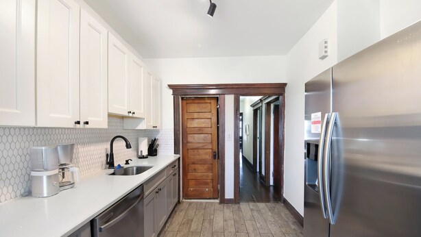 A kitchen with white cabinets, stainless steel appliances, a wooden door, and a tiled backsplash. - Newly Updated 3BR Furnished Home Close to Path, Lightrail and Pets Welcome (Jersey City)