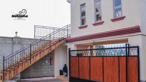 A hotel entrance with a wooden staircase leading up to a gated driveway. - Nataaha Hotels (Mbarara)