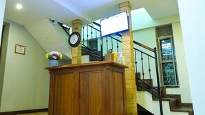 A staircase with a wooden handrail, a clock on the wall, and a flower vase on a pedestal. - Nataaha Hotels (Mbarara)