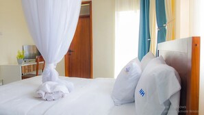 A neatly made bed with a white canopy, a wooden headboard, and pillows with a logo. - Nataaha Hotels (Mbarara)