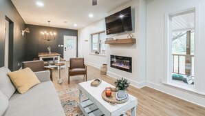 A modern living room with a sofa, chairs, a coffee table, a fireplace, a TV, and a ceiling fan.