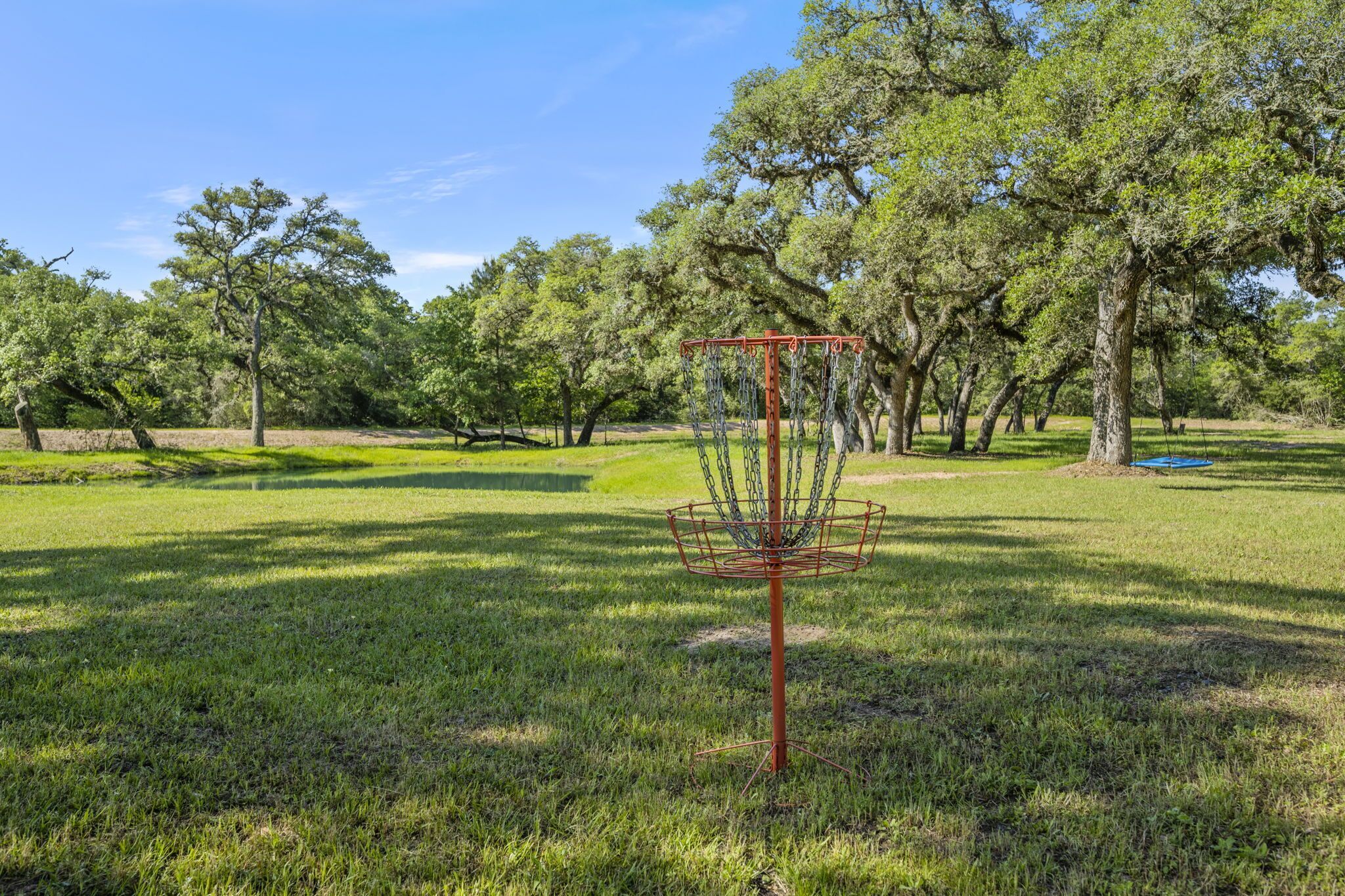 A disc golf basket in a park with trees and grass.