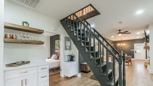 A modern kitchen with white cabinetry, a wooden countertop, and a black staircase with a wooden handrail.