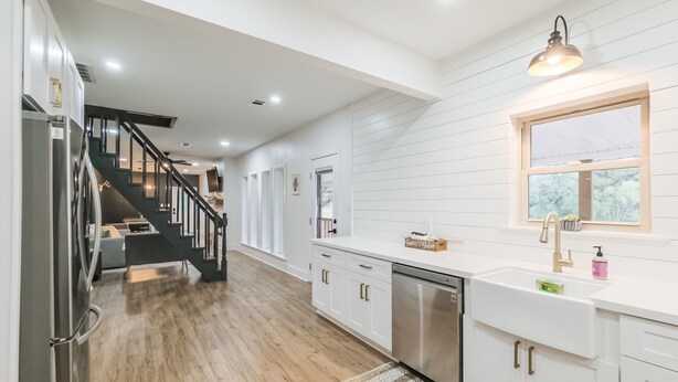 A modern kitchen with white cabinetry, a stainless steel dishwasher, and a wooden floor.
