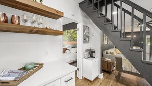 A modern kitchen with wooden shelves, a coffee machine, and a dining area with a staircase.