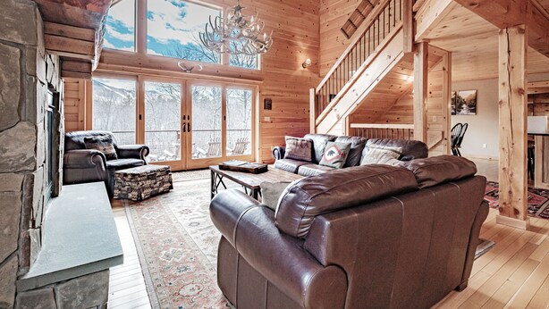 A spacious living room with a large brown leather sofa, a stone fireplace, and a wooden staircase leading to an upper level. - Spring & Summer Specials (Newry)