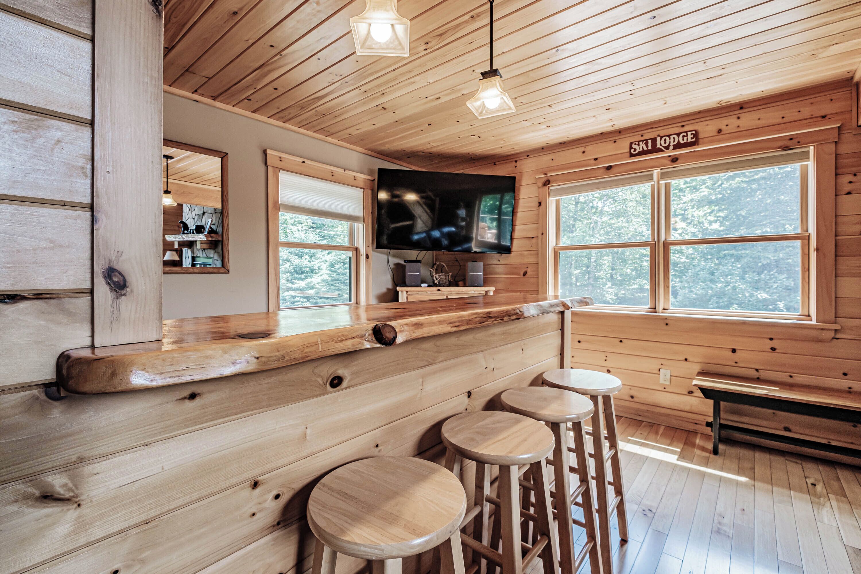 Um interior de madeira com área de bar, uma televisão fixada na parede e um letreiro com a inscrição 'Ski Lodge'.