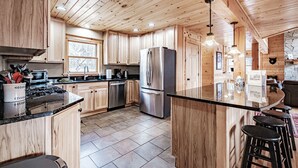 A spacious kitchen with wooden cabinets, a stainless steel refrigerator, and a large island with stools. - Spring & Summer Specials (Newry)