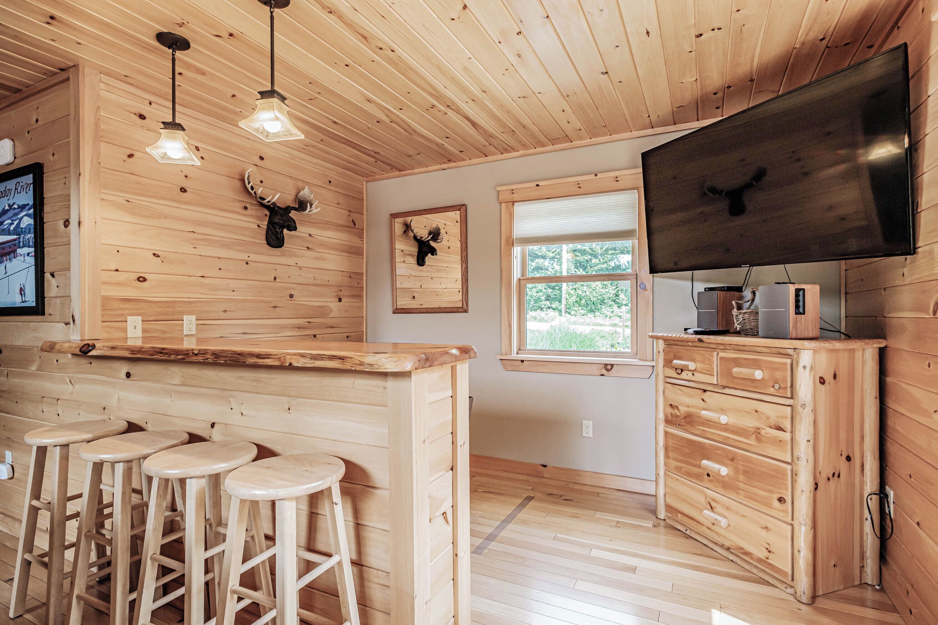 A wooden interior with a bar area, stools, a television, and mounted animal heads.
