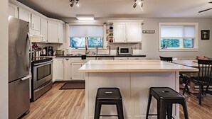 Une cuisine moderne avec des meubles blancs, des appareils en acier inoxydable et un îlot central doté de tabourets.