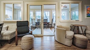 Un salon spacieux doté d’un plancher en bois, d’un canapé, d’un fauteuil et d’une table. Une porte-fenêtre coulissante donne sur un coin repas équipé d’une table et de chaises.
