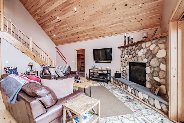 A cozy living room with a stone fireplace, wooden ceiling, and a leather sofa.