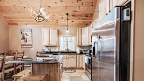 A kitchen with wooden cabinets, a stainless steel refrigerator, a wooden dining table with benches, and a chandelier.