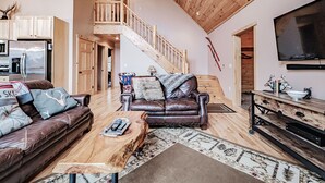 A spacious living area with a brown leather sofa, a wooden coffee table, and a TV mounted on the wall.