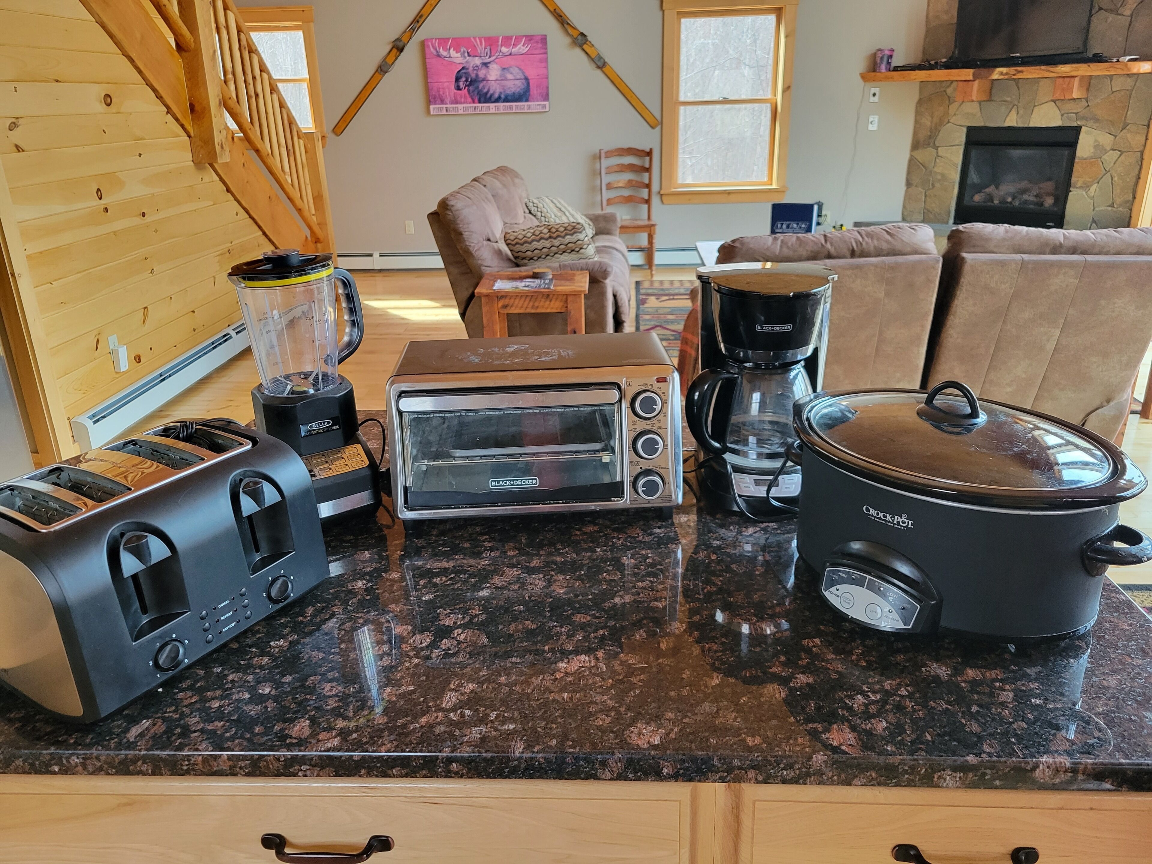 A kitchen with a granite countertop, a toaster, a coffee maker, a slow cooker, and a blender.