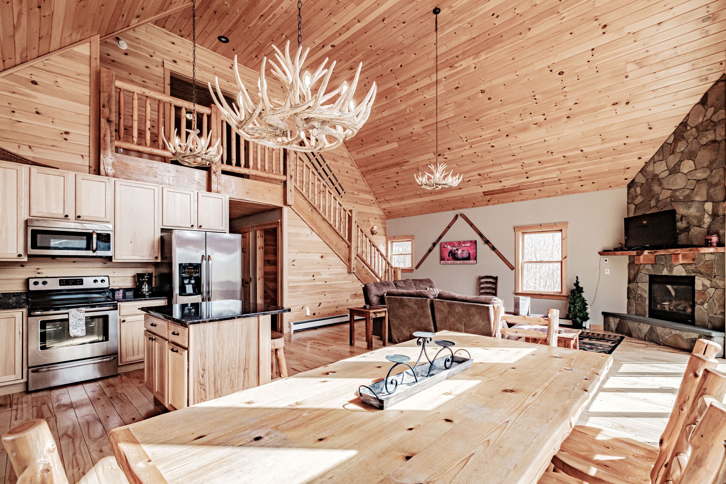 Ein geräumiger Holzraum mit großem Esstisch, Küchenzeile und Kamin aus Stein.