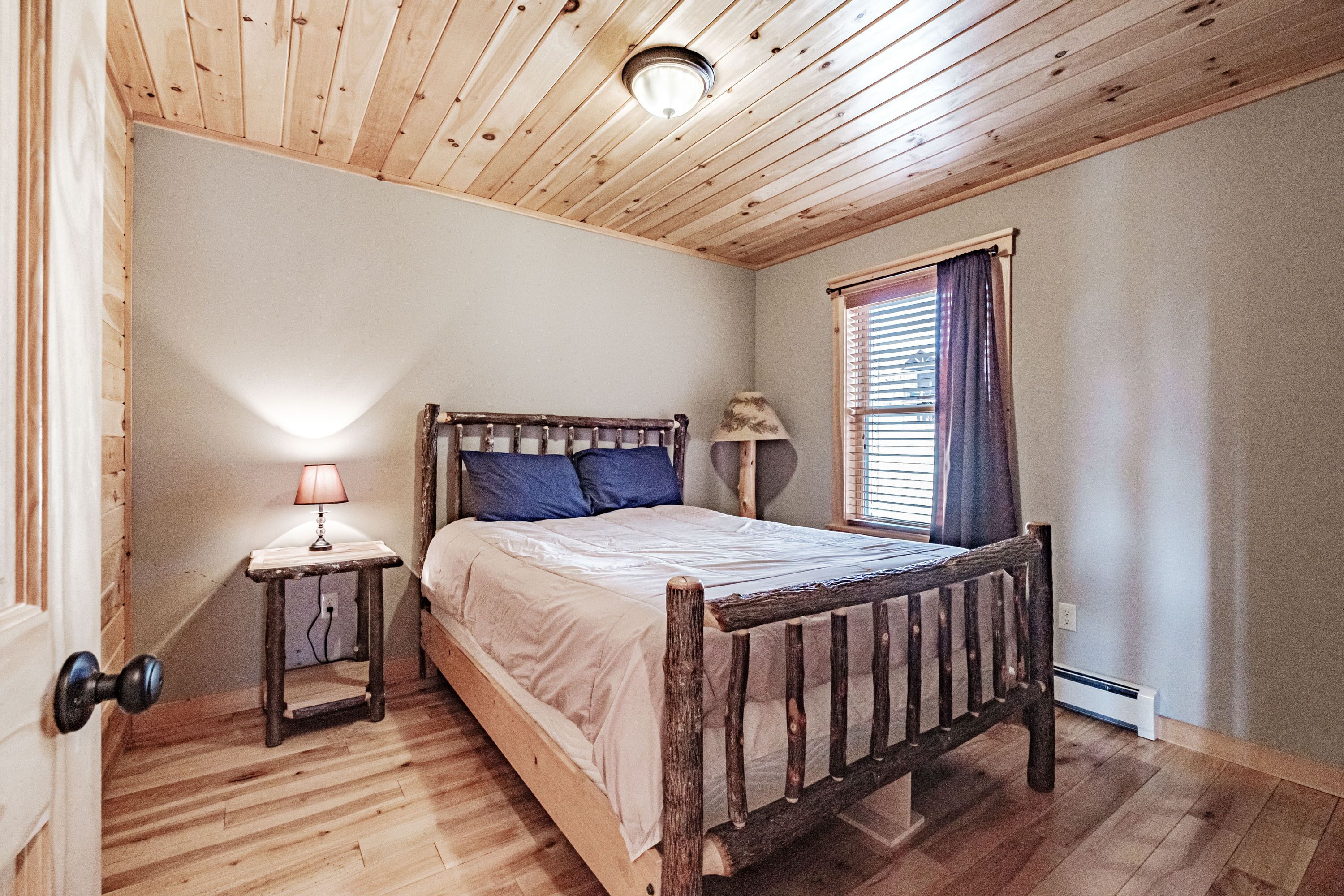 Une chambre à coucher avec un lit en bois, une table de chevet avec une lampe et une fenêtre avec des stores.
