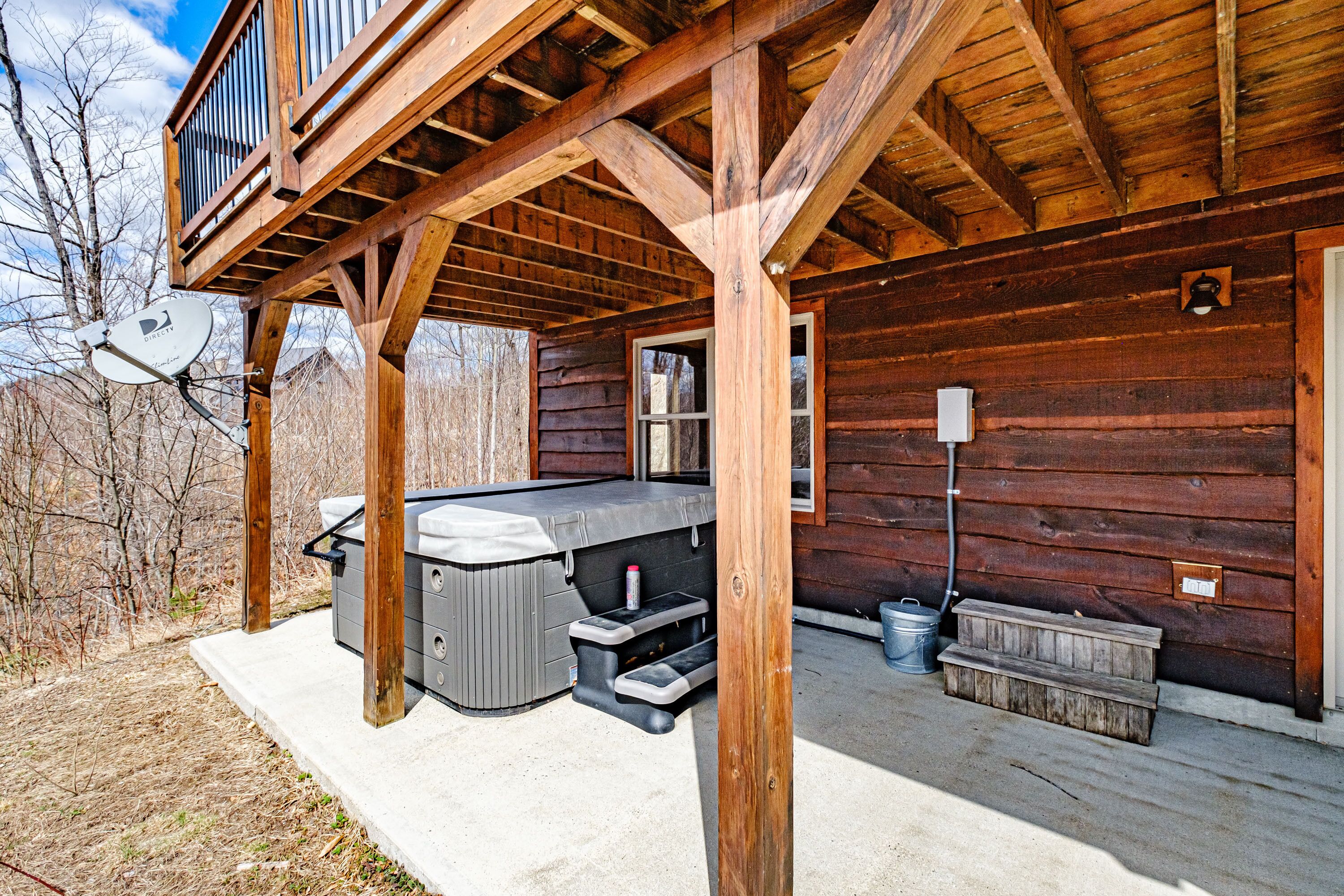 A wooden cabin with a hot tub, outdoor seating, and a satellite dish.
