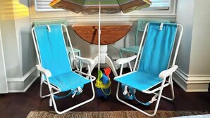 Een kamer met twee blauwe strandstoelen, een klein houten tafeltje en een kleurrijke, gestreepte parasol.