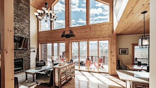 A spacious living area with a stone fireplace, wooden furniture, and large windows offering mountain views. - 2 miles within Sunday river, mountain side house (Newry)