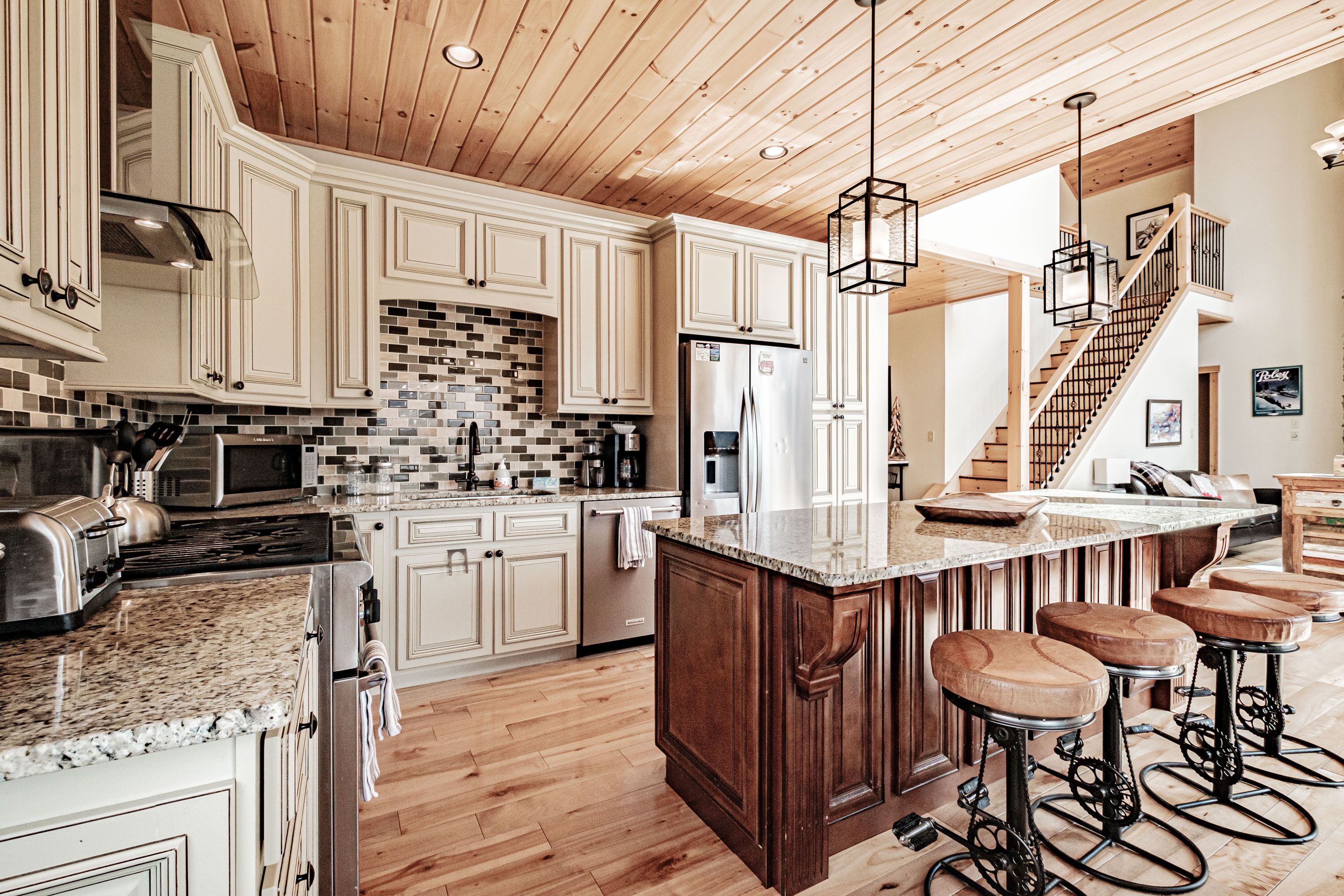 Een moderne keuken met houten plafond, granieten aanrecht en een centraal eiland met barstoelen.