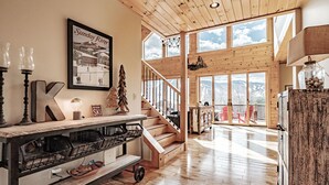 A spacious room with a wooden staircase, a large window with a view of mountains, and a framed picture on the wall. - 2 miles within Sunday river, mountain side house (Newry)