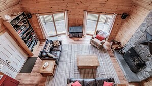 Un accogliente interno di una baita con pavimento in legno, camino, divano, tavolino da caffè e libreria.